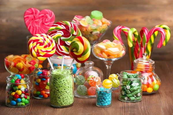 Colorful candies in jars on table on wooden background — Stock Photo, Image