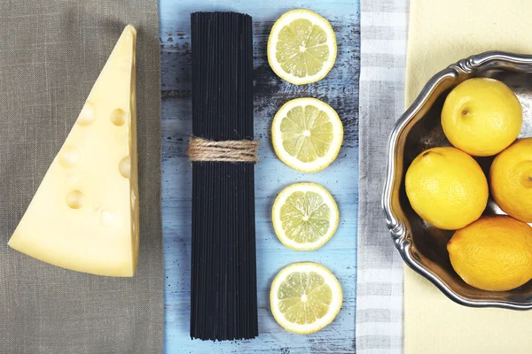 Formaggio, spaghetti neri e limoni sul tavolo in legno vista dall'alto — Foto Stock
