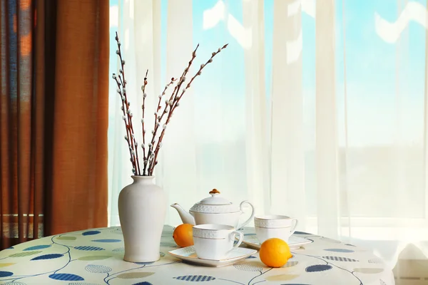 Willow takjes in vaas met theepot, bekers en citroen op tafel op gordijnen achtergrond — Stockfoto