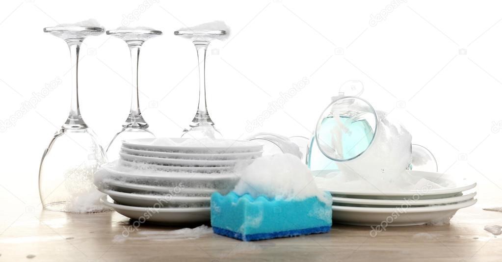 Dishes in foam with gloves and wisp on table isolated on white