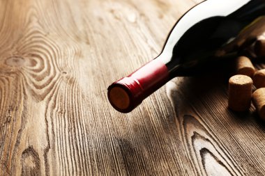 Ahşap masa arkasında mantarlı cam şarap şişesi.