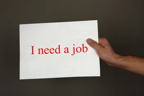 Blad papier met inscriptie ibehoefte een baan in mannenhand op donkere achtergrond — Stockfoto