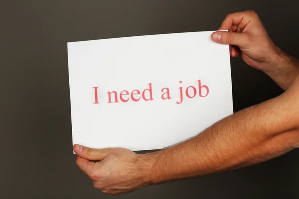 Blad papier met inscriptie ibehoefte een baan in mannelijke handen op donkere achtergrond — Stockfoto