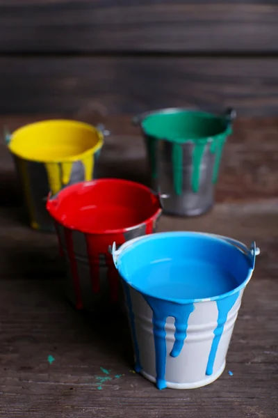 Metal buckets with colorful paint on wooden background — Stock Photo, Image