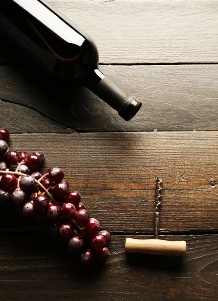 Skleněná láhev vína s vývrtkou a hrozny na dřevěný stůl pozadí — Stock fotografie