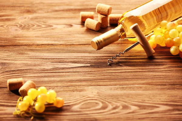 Glass bottle of wine with corks, corkscrew and grapes on wooden table background — Stock Photo, Image