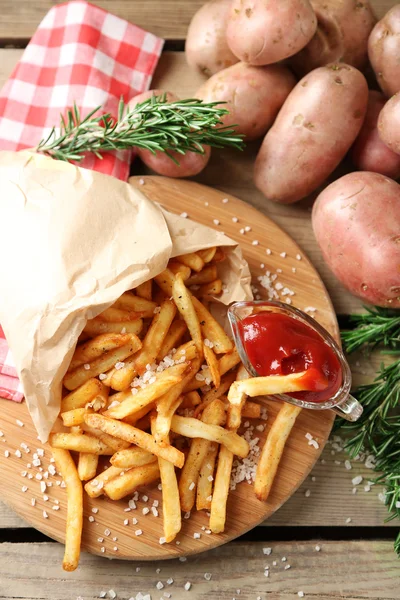 Batatas fritas saborosas na tábua de corte, no fundo da mesa de madeira — Fotografia de Stock