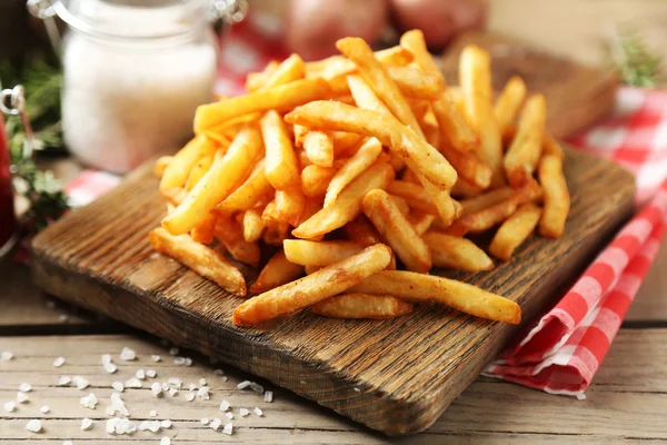 Tasty french fries on cutting board, on wooden table background