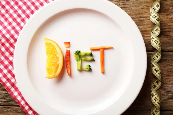 Word DIET made of sliced vegetables in plate with measuring tape on wooden table, top view — Stock Photo, Image