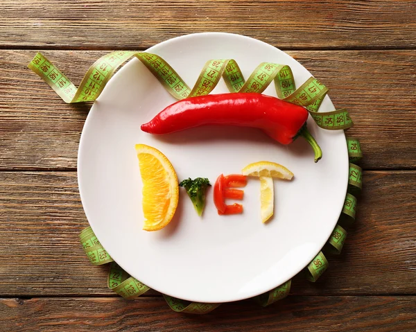 Word DIET made of sliced vegetables in white plate with measuring tape on wooden table, top view — Stock Photo, Image