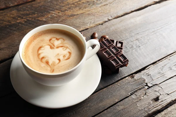 Tasse de café latte art avec des grains et du chocolat sur fond en bois — Photo