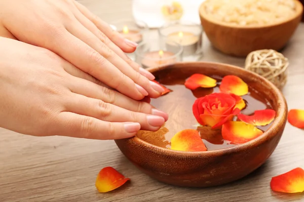 Manos femeninas y tazón de agua de spa con flores, primer plano — Foto de Stock