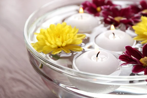 Tigela de água termal com flores e velas em mesa de madeira, close-up — Fotografia de Stock