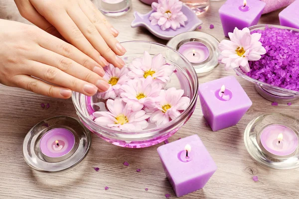 Mains féminines avec bol d'eau de spa aromatique sur table en bois, gros plan — Photo