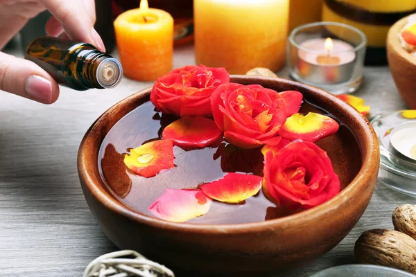 Vrouwelijke hand met fles essentie en kom van het aroma spa water op houten tafel, close-up — Stockfoto
