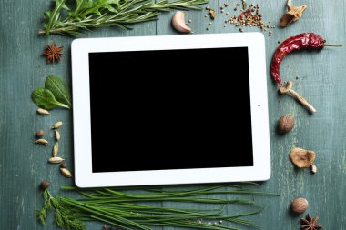 Dijital tablet ile taze otlar ve baharatlar ahşap arka plan üzerinde