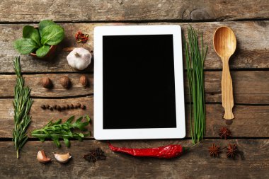 Dijital tablet ile taze otlar ve baharatlar ahşap arka plan üzerinde