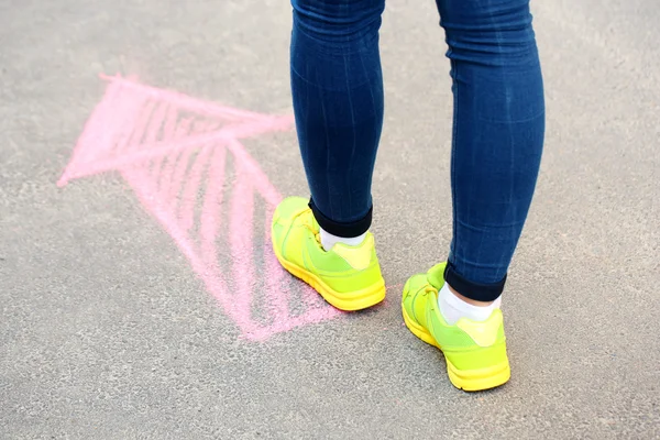 Kvinnliga fötter och ritade pil på trottoaren bakgrund — Stockfoto