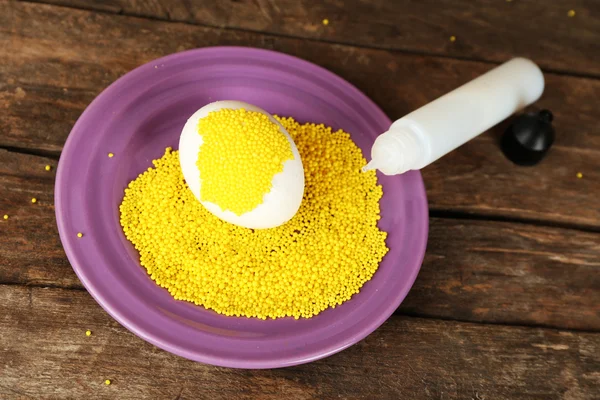 Decorating Easter egg on color plate on wooden table, closeup — Stock Photo, Image