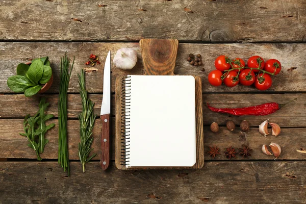 Livro de receitas aberto com ervas frescas, tomates e especiarias em fundo de madeira — Fotografia de Stock