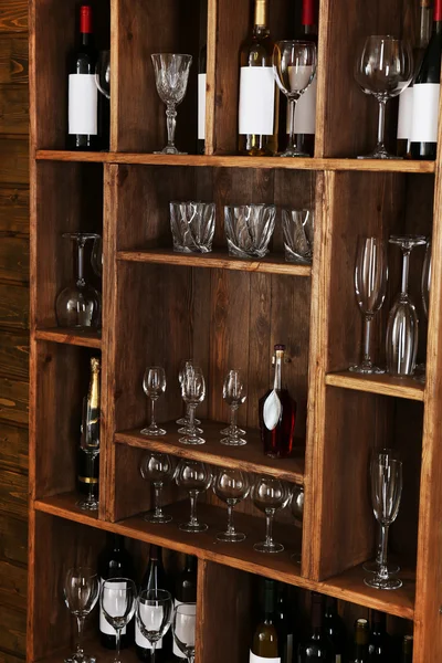 Shelving with wine bottles with glasses on wooden wall background — Stock Photo, Image