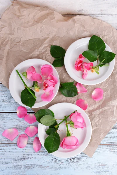 Schöne rosa Rosen in weißen Tellern auf Holztisch mit Pergament, Draufsicht — Stockfoto