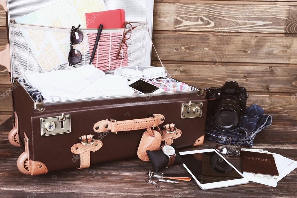 Packed suitcase of vacation items on wooden background