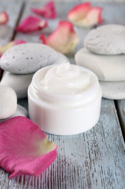 Gül yaprakları ve spa taşlar ahşap arka plan üzerinde kozmetik krem