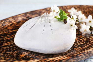 Akupunktur iğneleri çakıl ve çiçekli dal, closeup ile ahşap plaka üzerinde