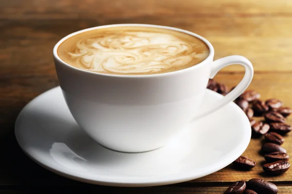Filiżanka do kawy latte art z ziarna na drewnianym stole, zbliżenie — Zdjęcie stockowe