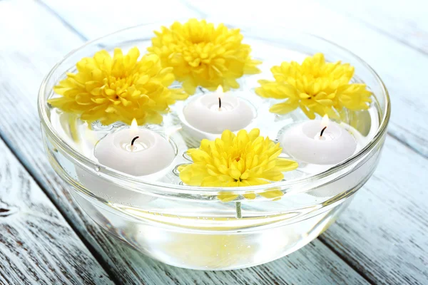 Bol d'eau de spa avec des fleurs et des bougies sur table en bois, gros plan — Photo