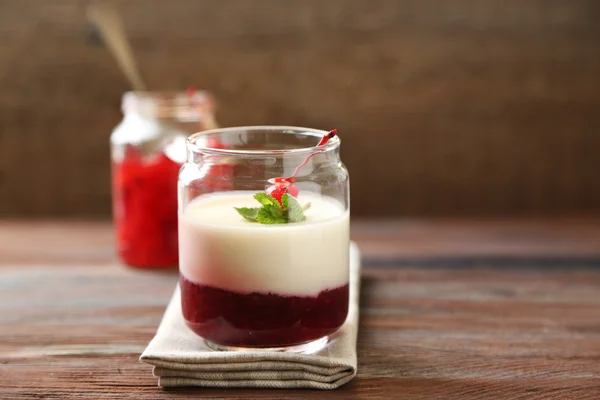 Frasco de vidro com saborosa sobremesa de panna cotta na placa, na mesa de madeira — Fotografia de Stock