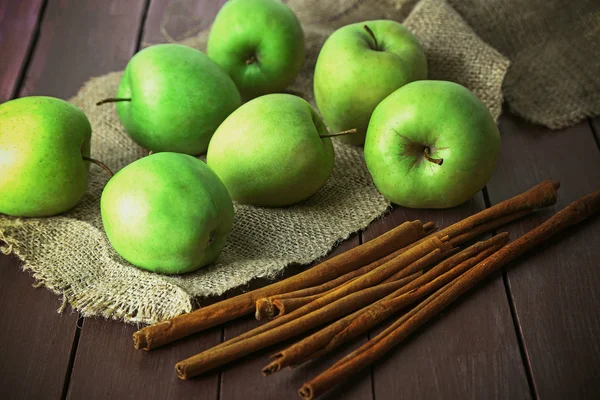 Maçãs verdes com paus de canela na mesa de madeira com pano de saco, close-up — Fotografia de Stock