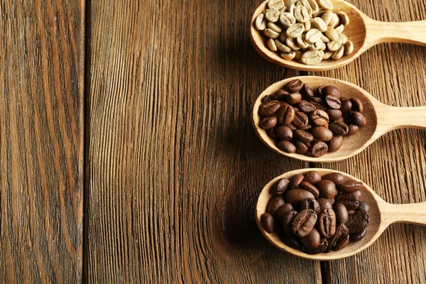 Kaffeebohnen in Löffeln auf Holzgrund — Stockfoto