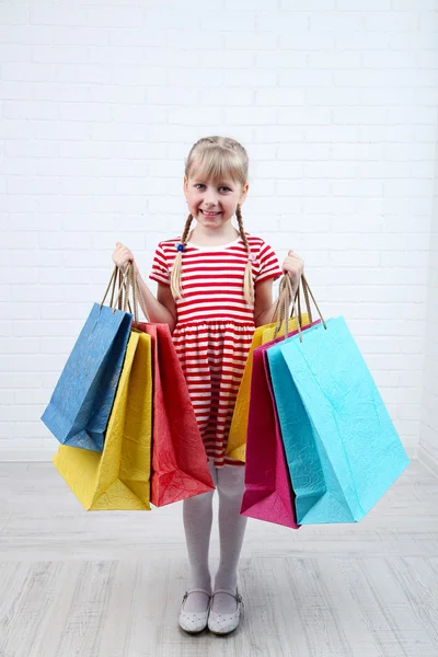 Beautiful little girl with shopping bags in room — Stock Photo, Image