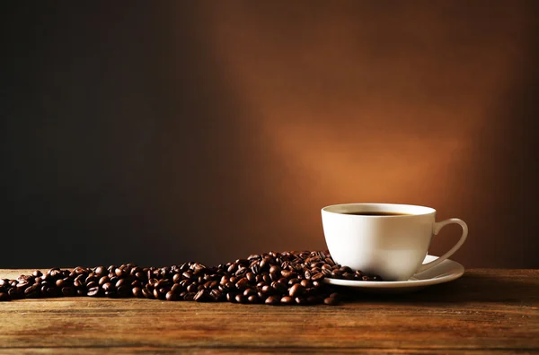 Kopje koffie met korrels op houten tafel op donkere achtergrond — Stockfoto