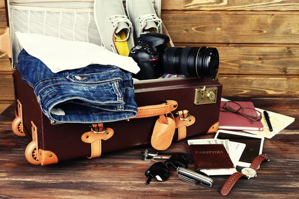 Maleta embalada de artículos de vacaciones sobre fondo de madera — Foto de Stock