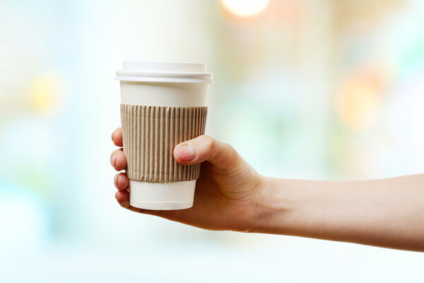 Hand holding paper cup of coffee on bright background