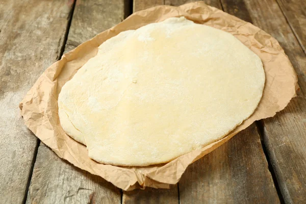 Rolled dough on paper on wooden background — Stock Photo, Image