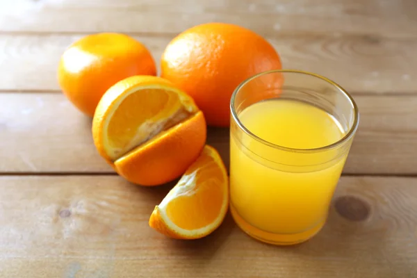 Glas apelsinjuice och skivor på träbord bakgrund — Stockfoto
