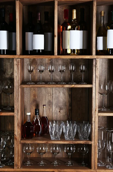 Shelving with wine bottles with glasses on wooden wall background — Stock Photo, Image