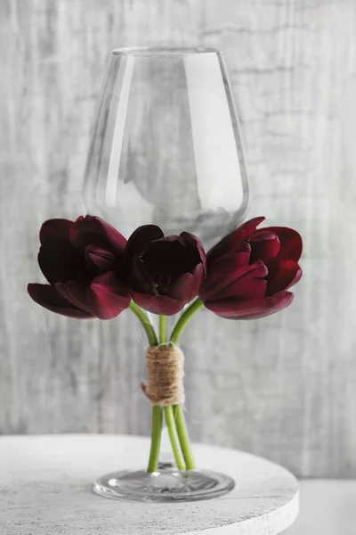 Nature morte avec verre et tulipes violettes sur fond de papier peint gris — Photo