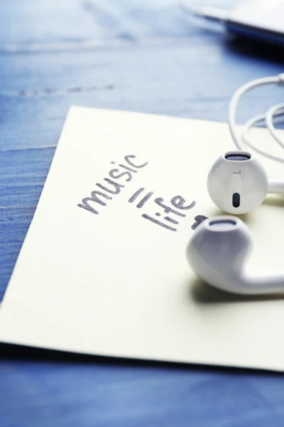 Koptelefoon met tekst muziek - leven op sticker op houten tafel, close-up — Stockfoto