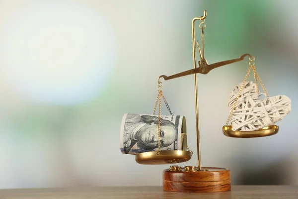 Money and heart in balance scales on light blurred background — Stock Photo, Image