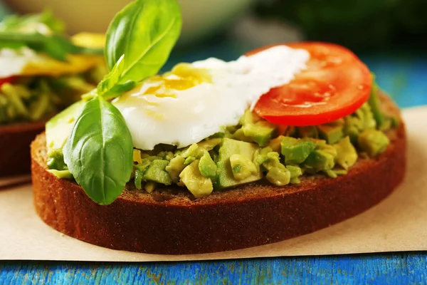 Tasty sandwich with egg, avocado and vegetables on paper napkin, on color wooden background — Stock Photo, Image