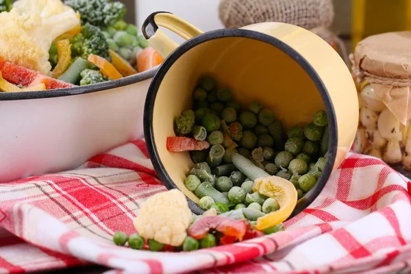 Verduras congeladas en tazón y taza en servilleta, sobre fondo de mesa de madera —  Fotos de Stock