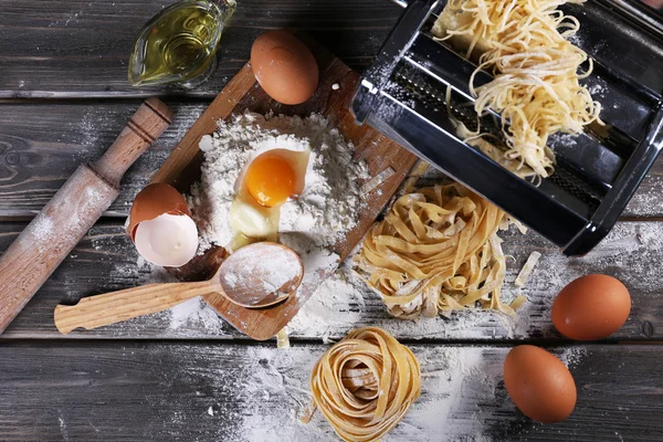 Máquina de hacer pasta de metal e ingredientes para pasta sobre fondo de madera —  Fotos de Stock