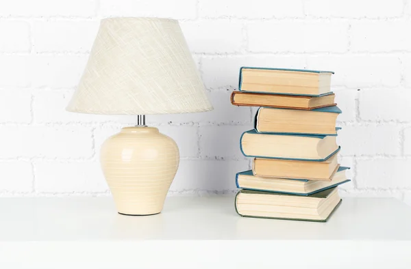 Wooden shelf with books and lamp on brick wall background — Stock Photo, Image