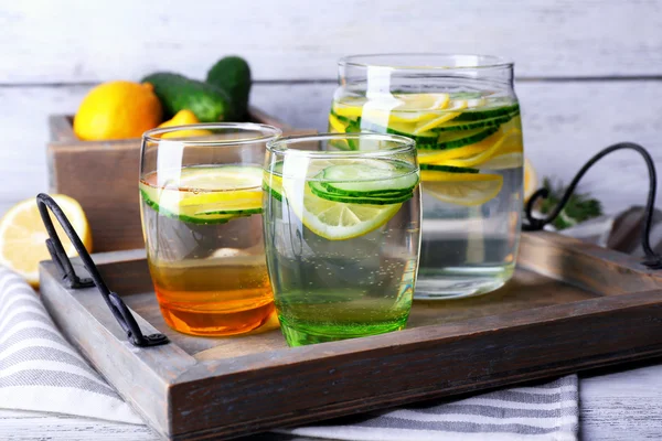 Agua dulce con limón y pepino en cristalería en bandeja de madera, primer plano —  Fotos de Stock