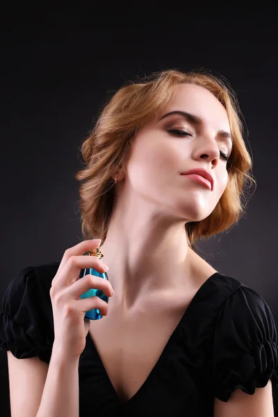 Krásná mladá žena s parfémy láhev na černém pozadí — Stock fotografie